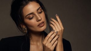 A beautiful young woman with Bella Hadid-inspired styling gazing at her freshly painted taupe nails with a look of quiet satisfaction, dramatic studio lighting, fashion editorial setting