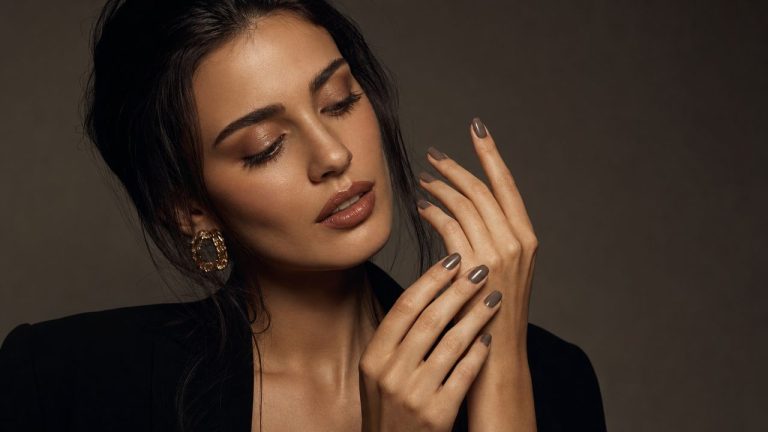 A beautiful young woman with Bella Hadid-inspired styling gazing at her freshly painted taupe nails with a look of quiet satisfaction, dramatic studio lighting, fashion editorial setting