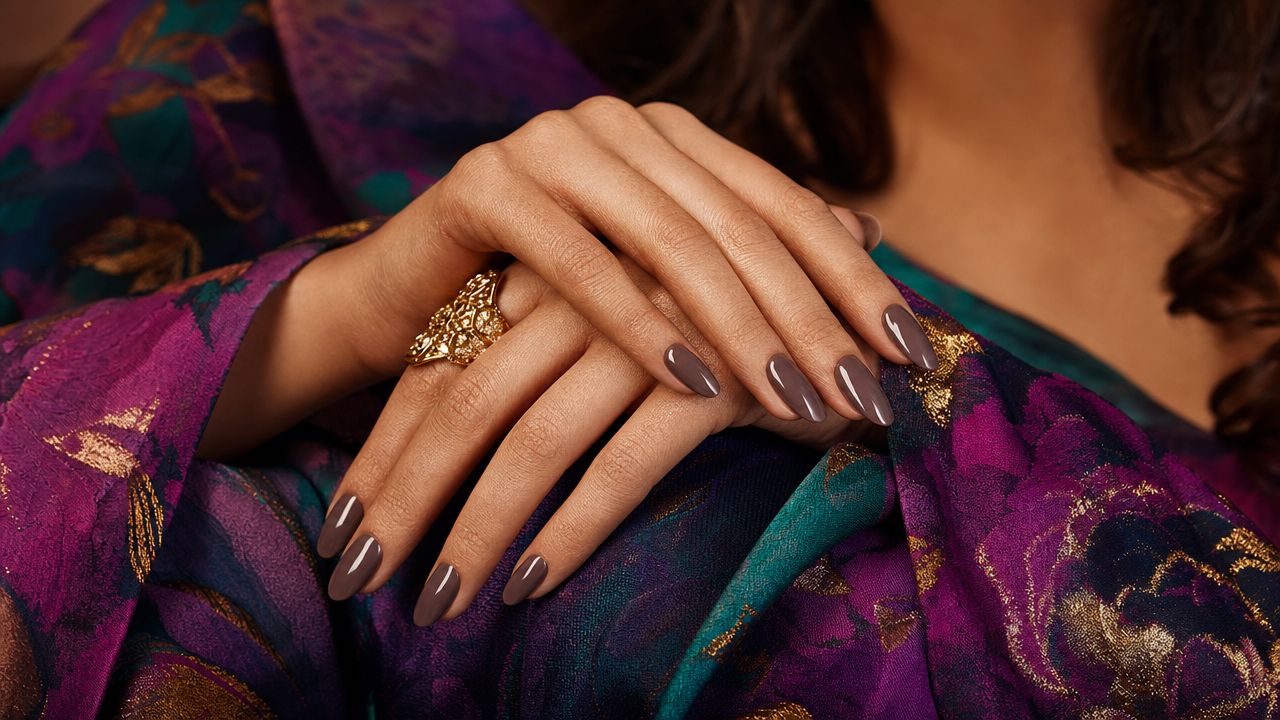 Close-up editorial shot of taupe painted nails against a bold fashion outfit, showcasing the contrast between the muted nail colour and vibrant clothing