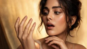 A beautiful woman with glossy, healthy nails holds her hand up close to her face, examining the base of her nails with a look of surprised curiosity, dramatic beauty editorial lighting