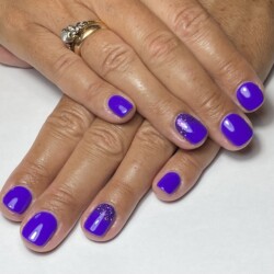 Estilizada em Glitters, a nail art representa a Galáxia/Espaço. Essas unhas curtas em formato oval foram criadas usando o sistema de esmalte em gel e são coloridas de roxo. 